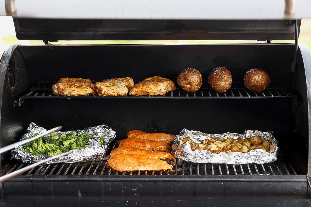 A smoker filled with smoked chicken breasts, broccoli, potatoes and chicken thighs. 