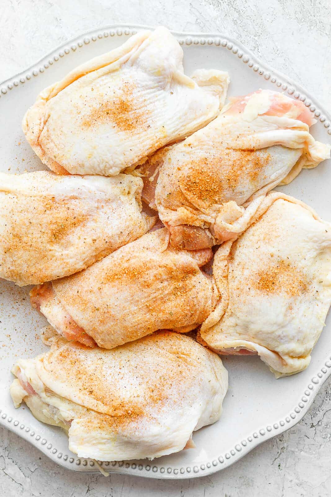 A plate of raw chicken thighs covered in a smoked chicken dry rub. 