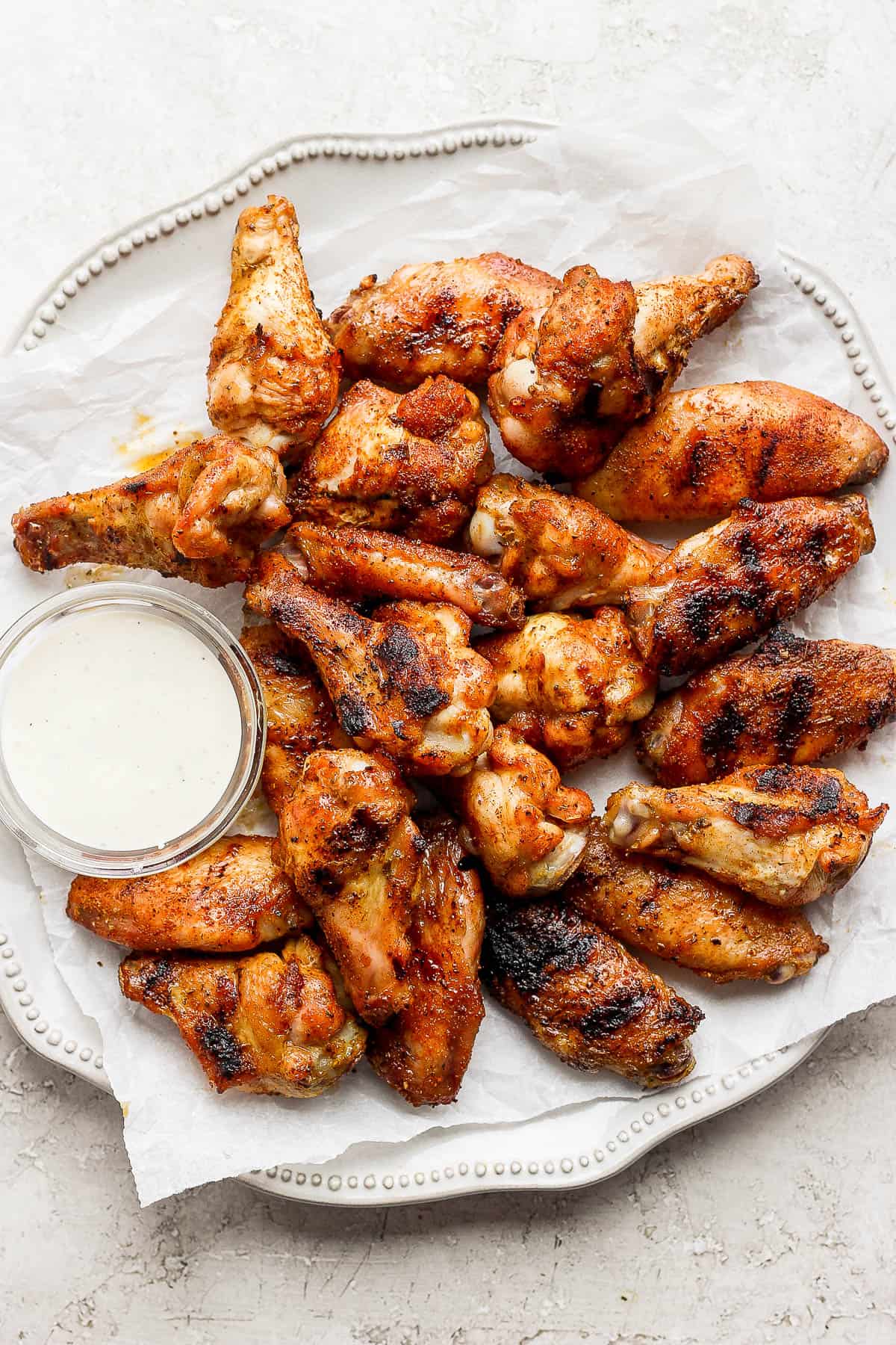 Smoked chicken wings on a plate with ranch dressing. 