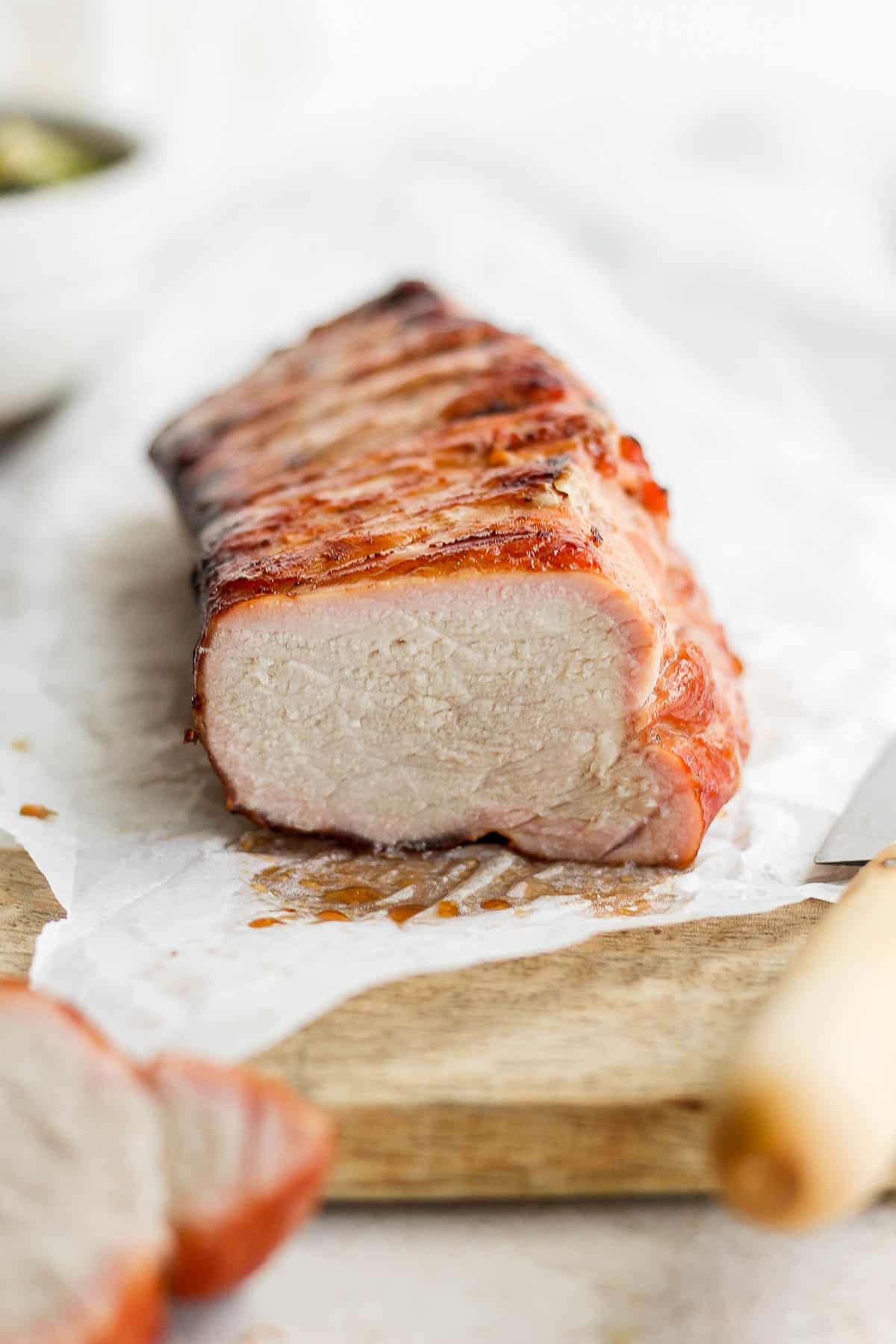 A smoked pork loin on a piece of parchment with the end cut off showing a juicy inside. 