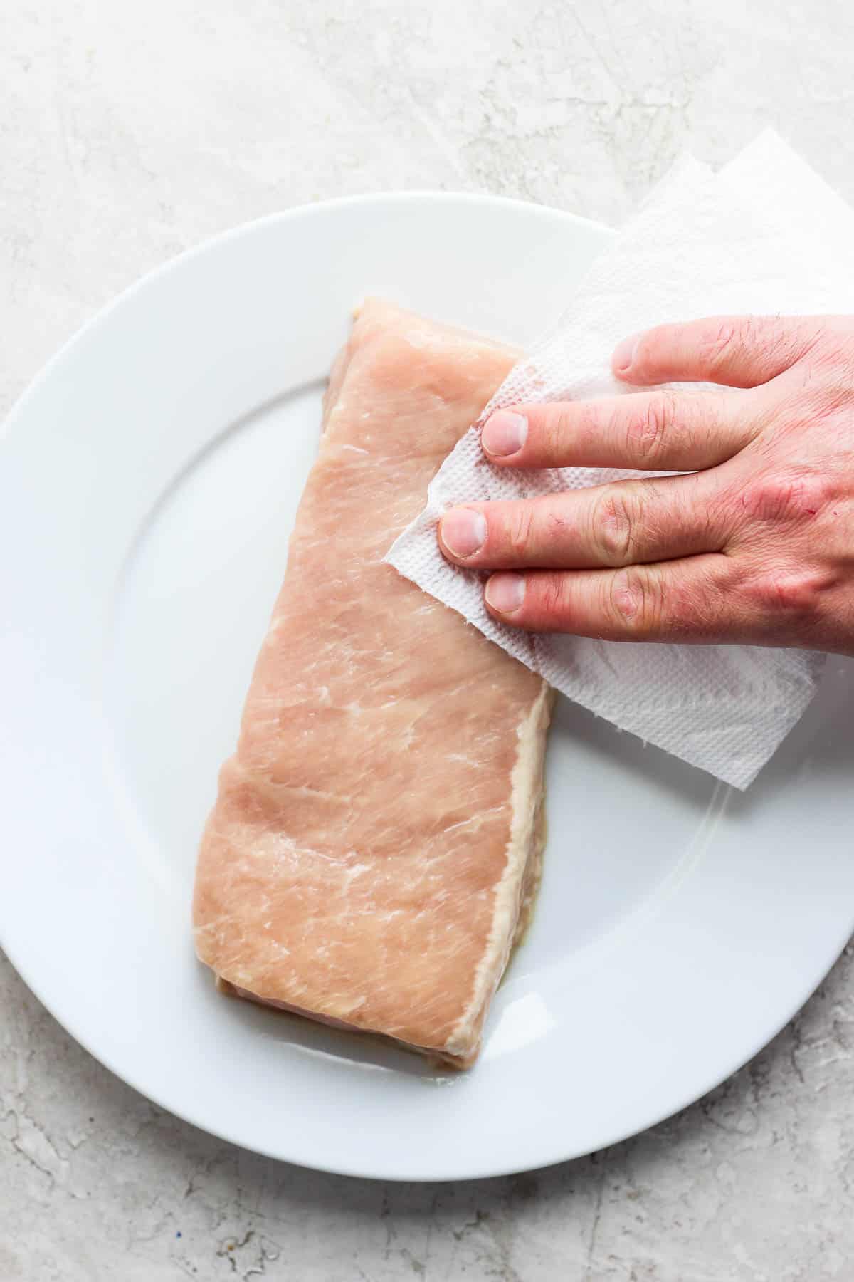 Someone patting dry a pork loin with a clean paper towel.