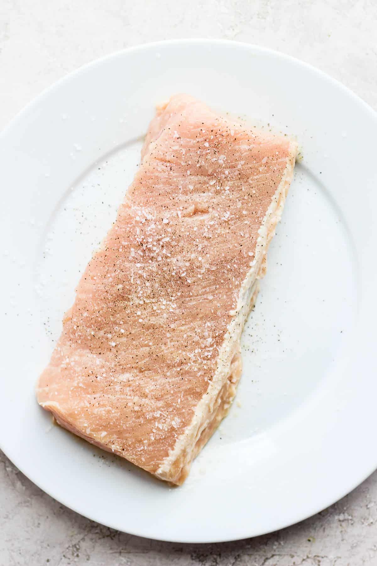 A raw pork loin seasoned with salt and pepper. 