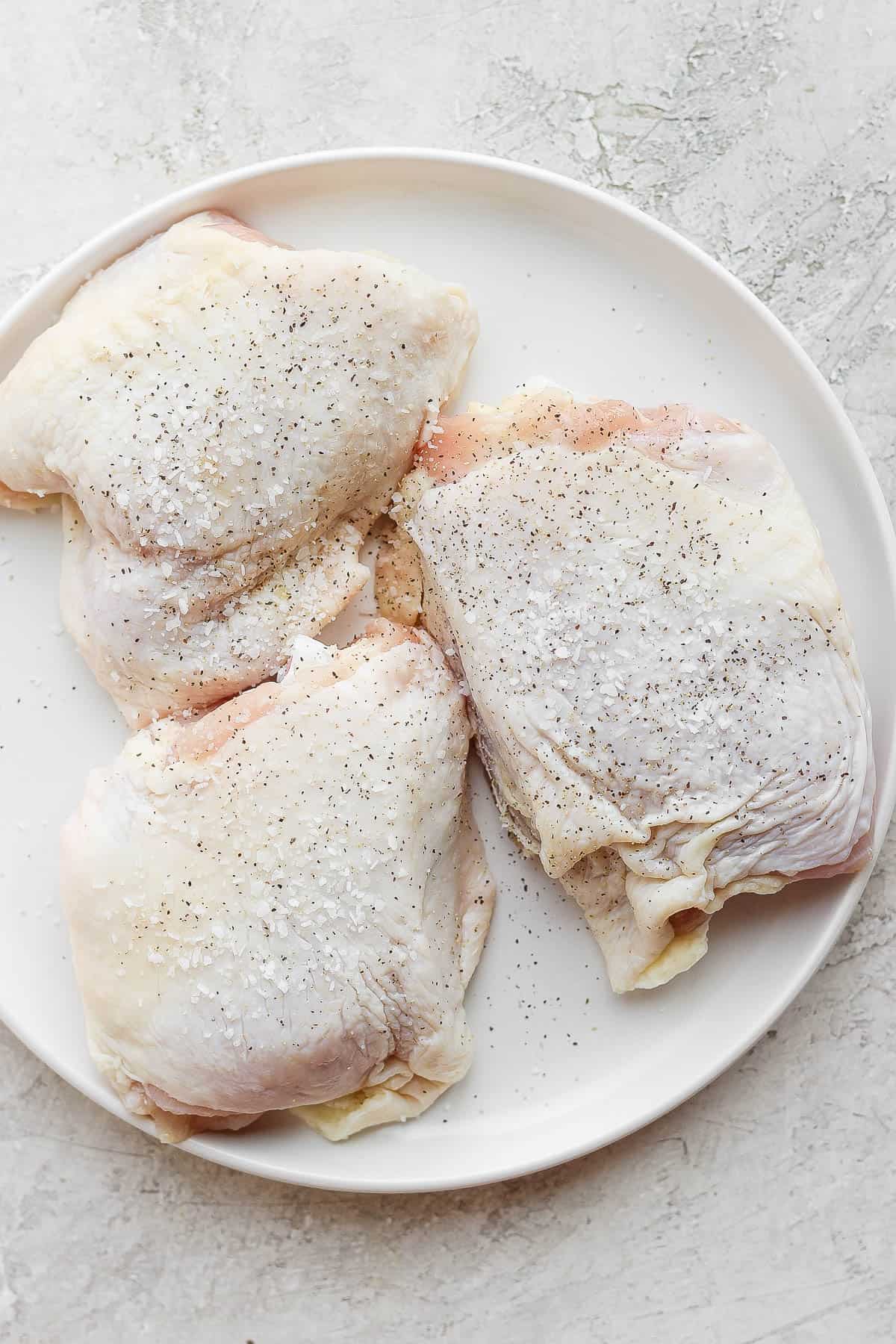 Raw chicken thighs seasoned and on a plate.