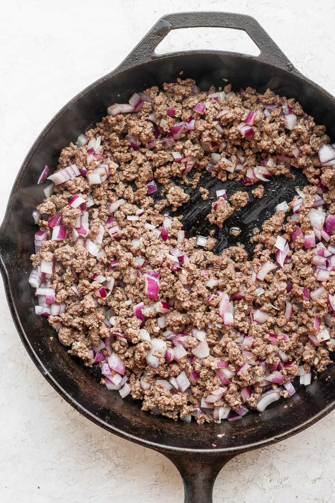 Ground beef with garlic and red onion in a cast iron skillet.