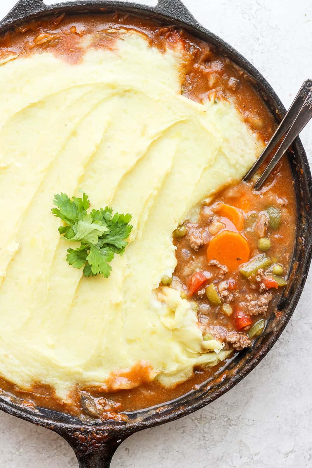 Shepherd's pie in a cast iron skillet with 2 spoons.