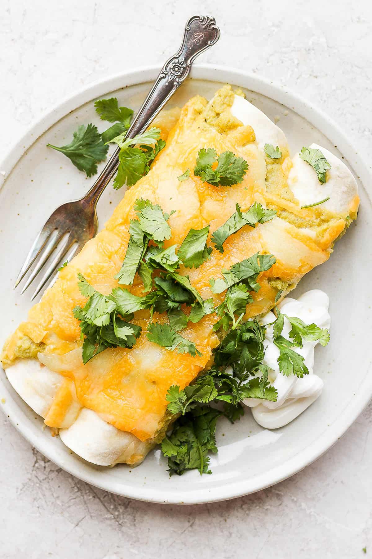 Two green chicken enchiladas on a plate with a fork.