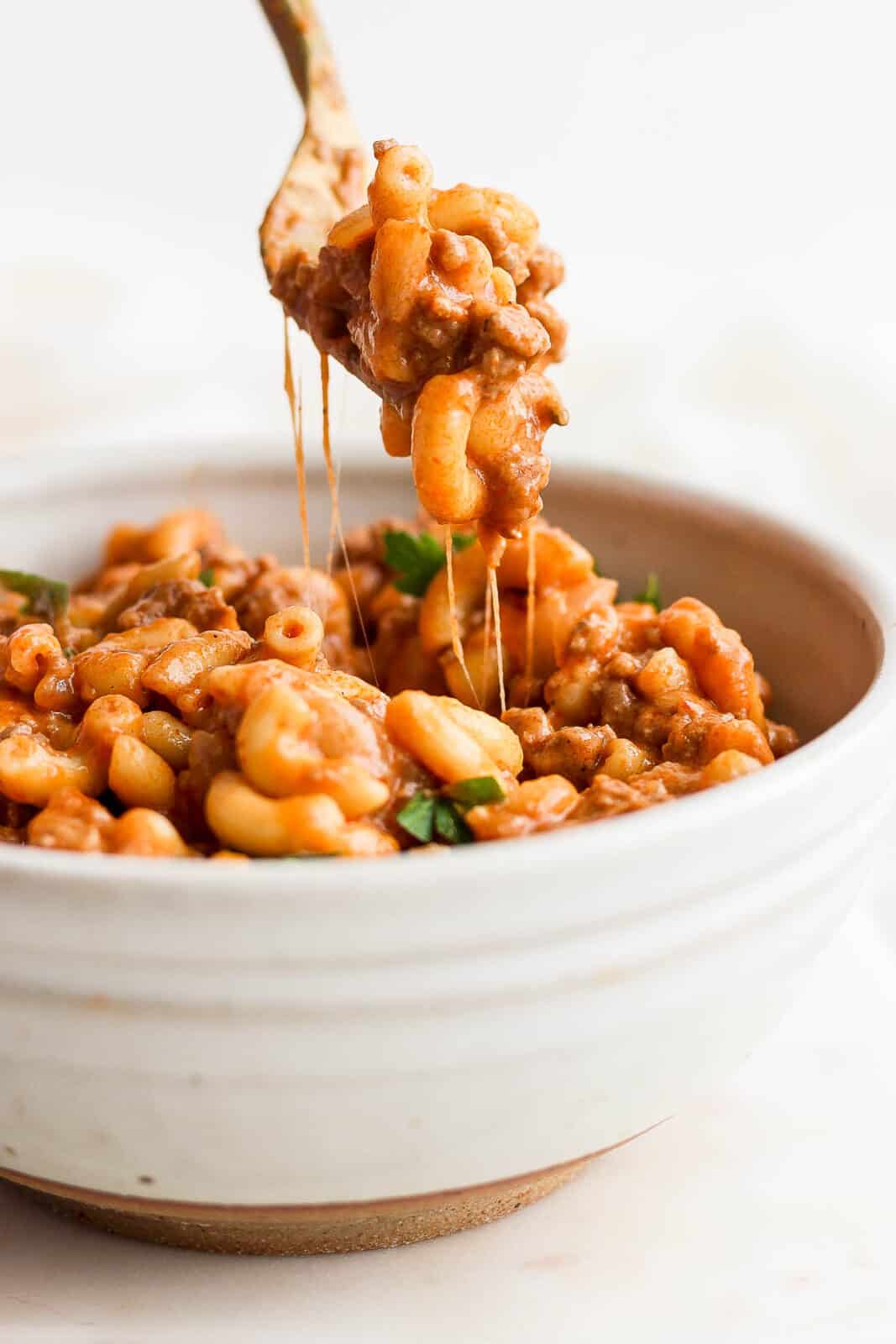 A fork pulling some hamburger helper out of the bowl.