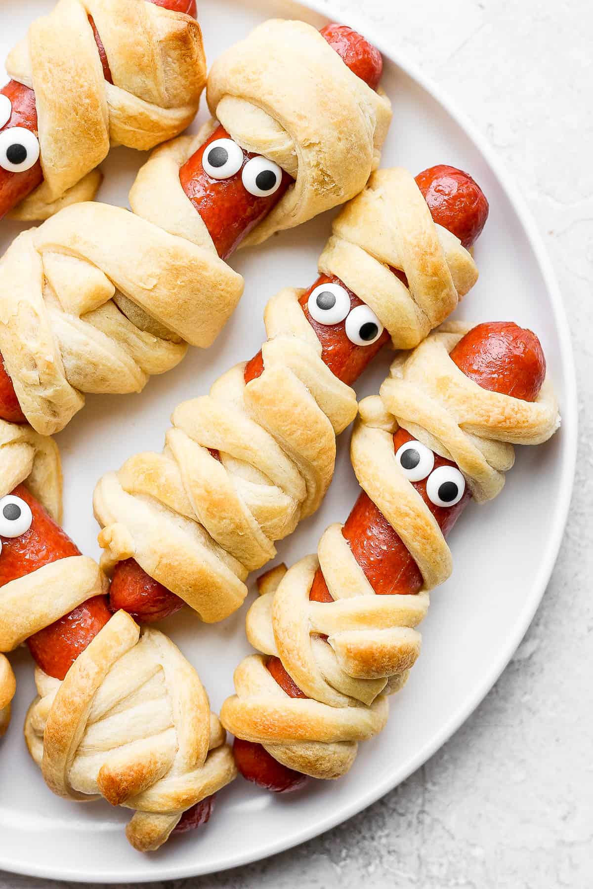 A white plate full of Mummy Hot Dogs with candy eyes.