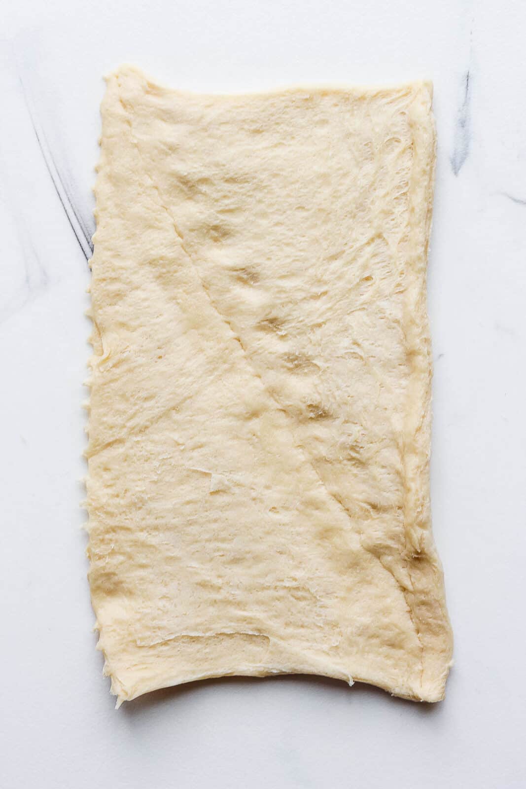 A piece of store-bought crescent roll dough with the seam pinched together to make one bigger piece.