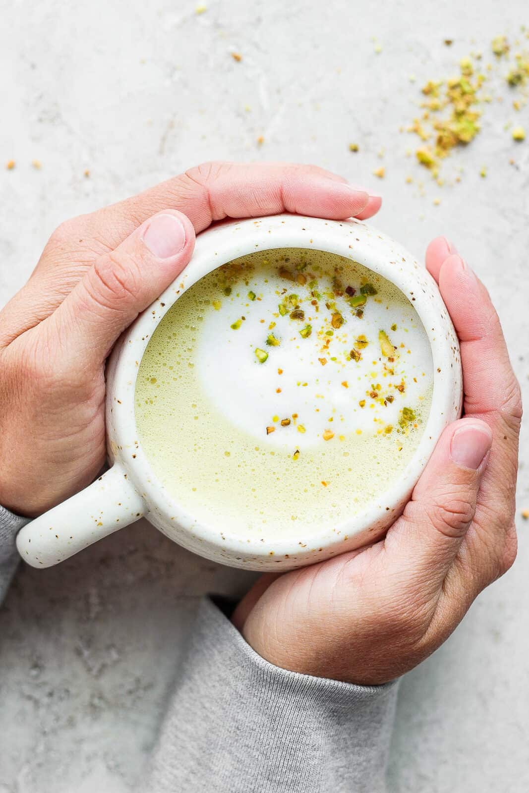 Hands holding a pistachio latte in a mug.
