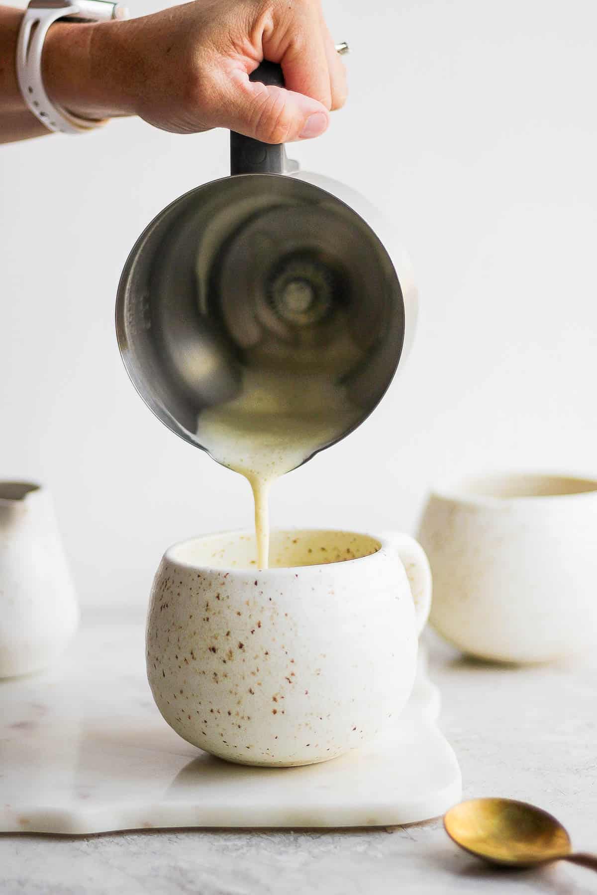 Pouring frothed pistachio milk on top of coffee in a mug.