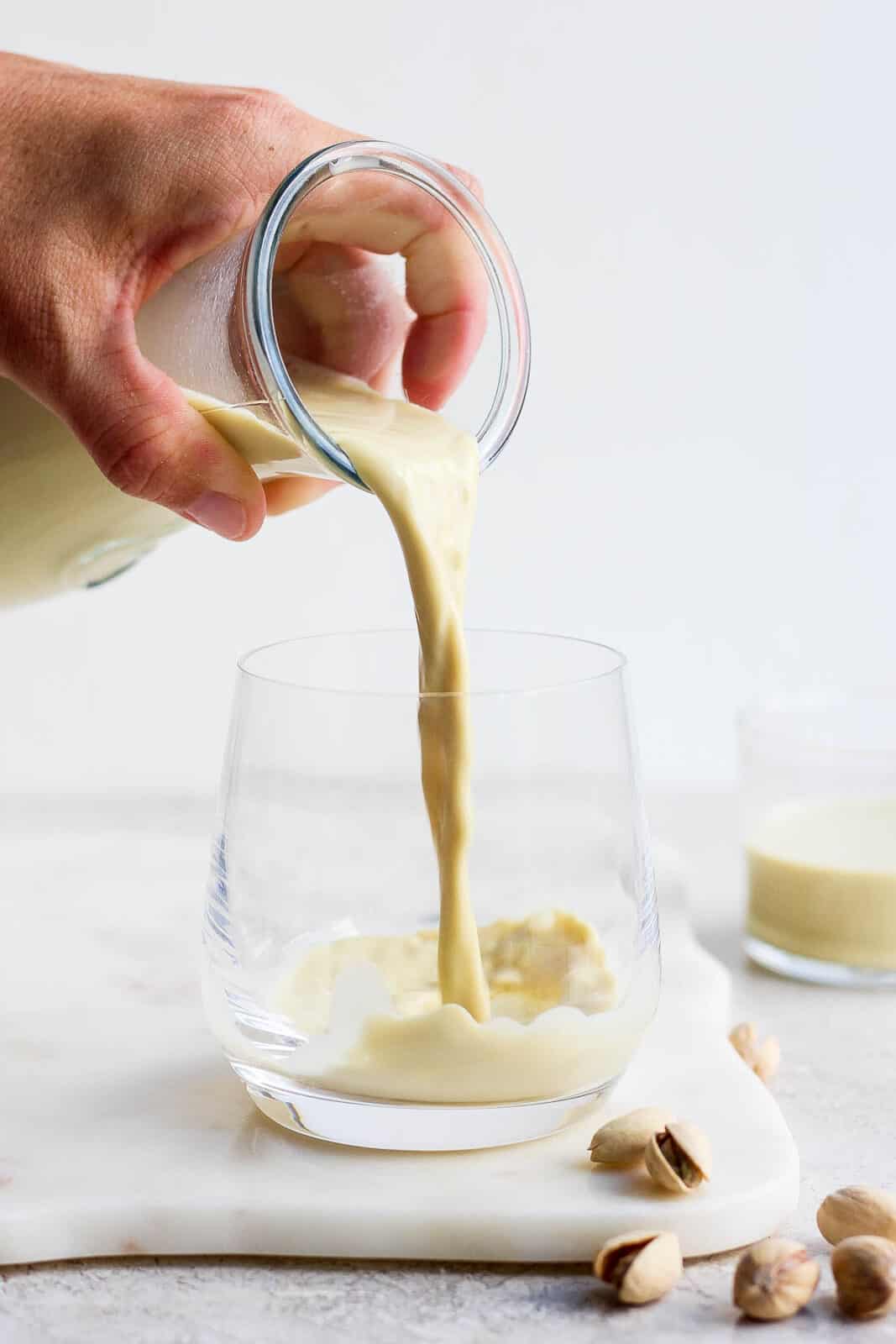 Pouring pistachio milk from a carafe into a glass.