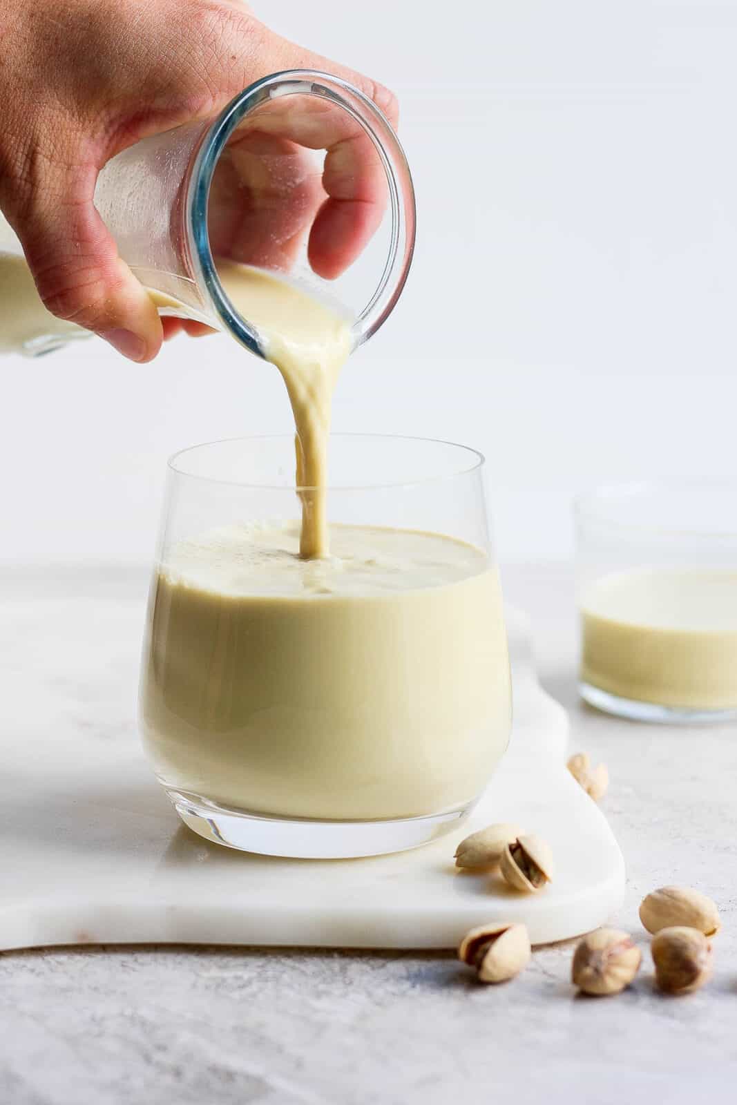 Pouring pistachio milk from a carafe to a glass.
