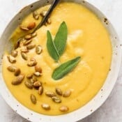 Bowl of acorn squash soup with pepitas and fresh sage leaves.