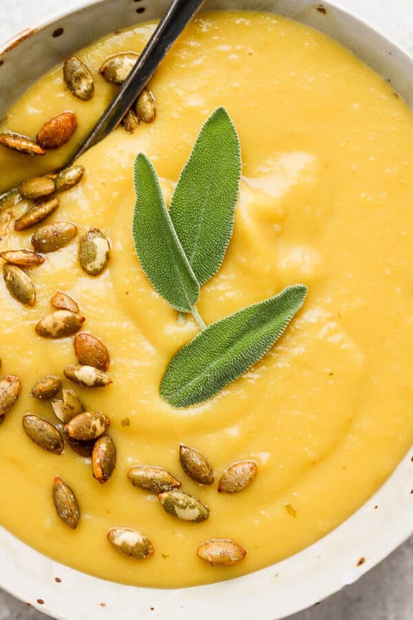 Bowl of acorn squash soup with pepitas and fresh sage leaves.