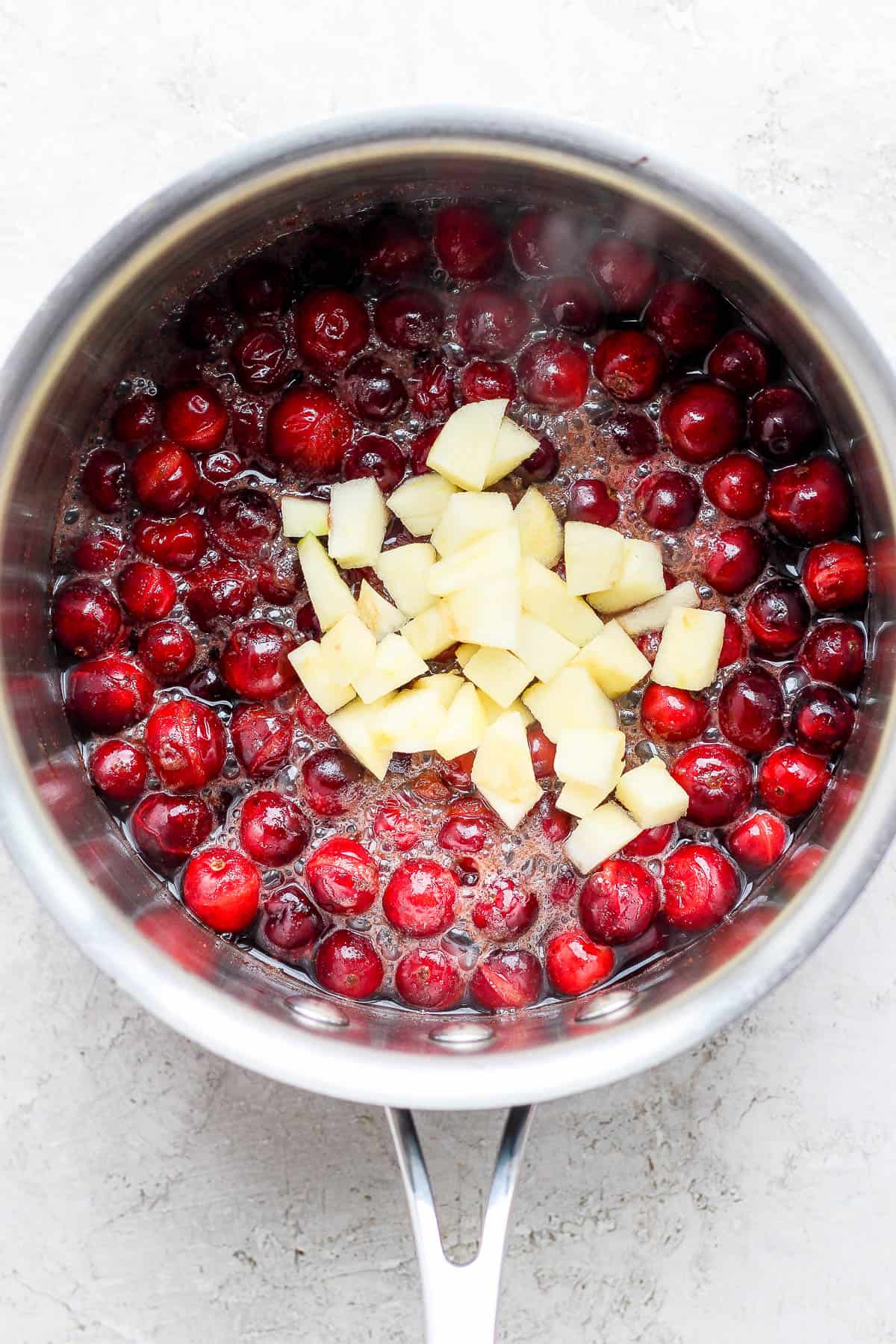 Apples added to apple cranberry sauce in a saucepan.