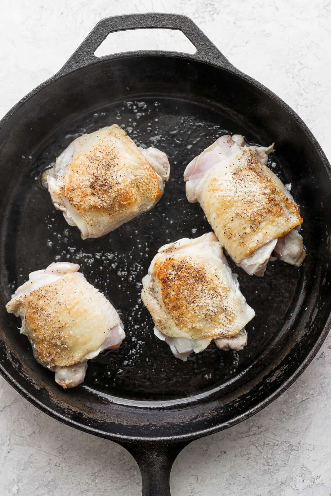 Chicken thighs searing in a cast iron skillet.