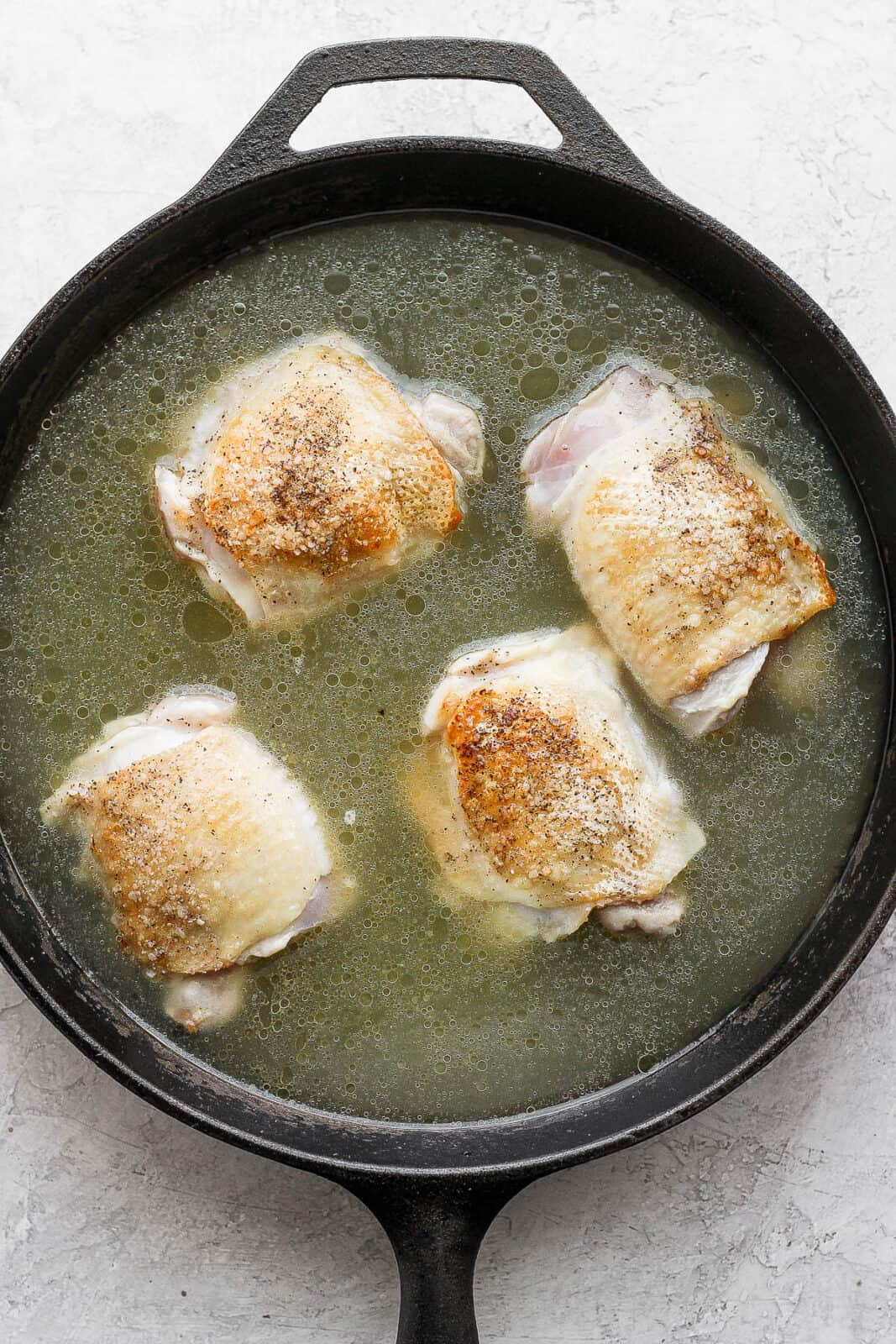 Chicken thighs in a skillet with broth.