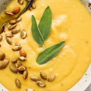 Bowl of acorn squash soup with pepitas and fresh sage leaves.