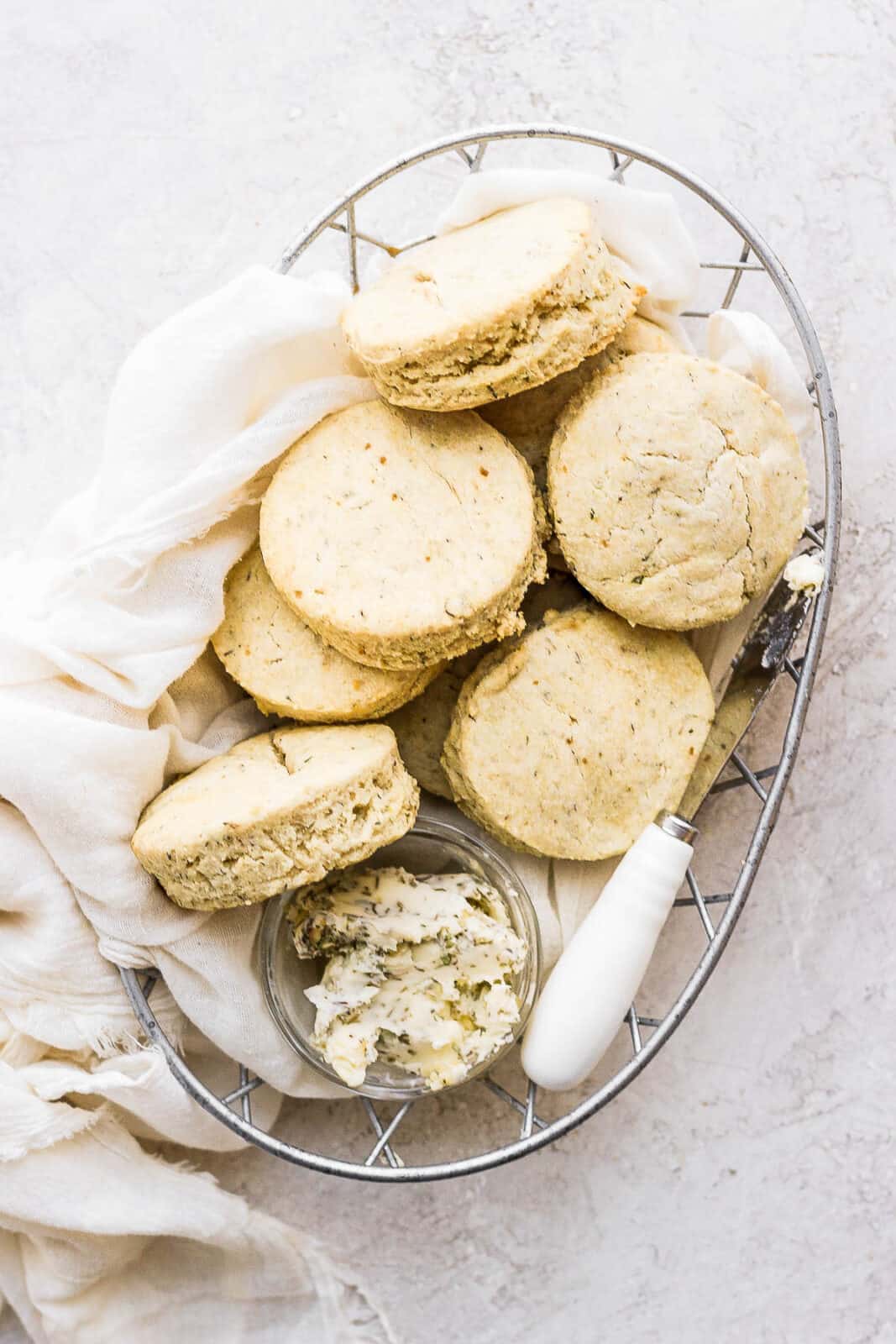 Gluten free biscuits in a basket with a small dish of herbed butter spread.