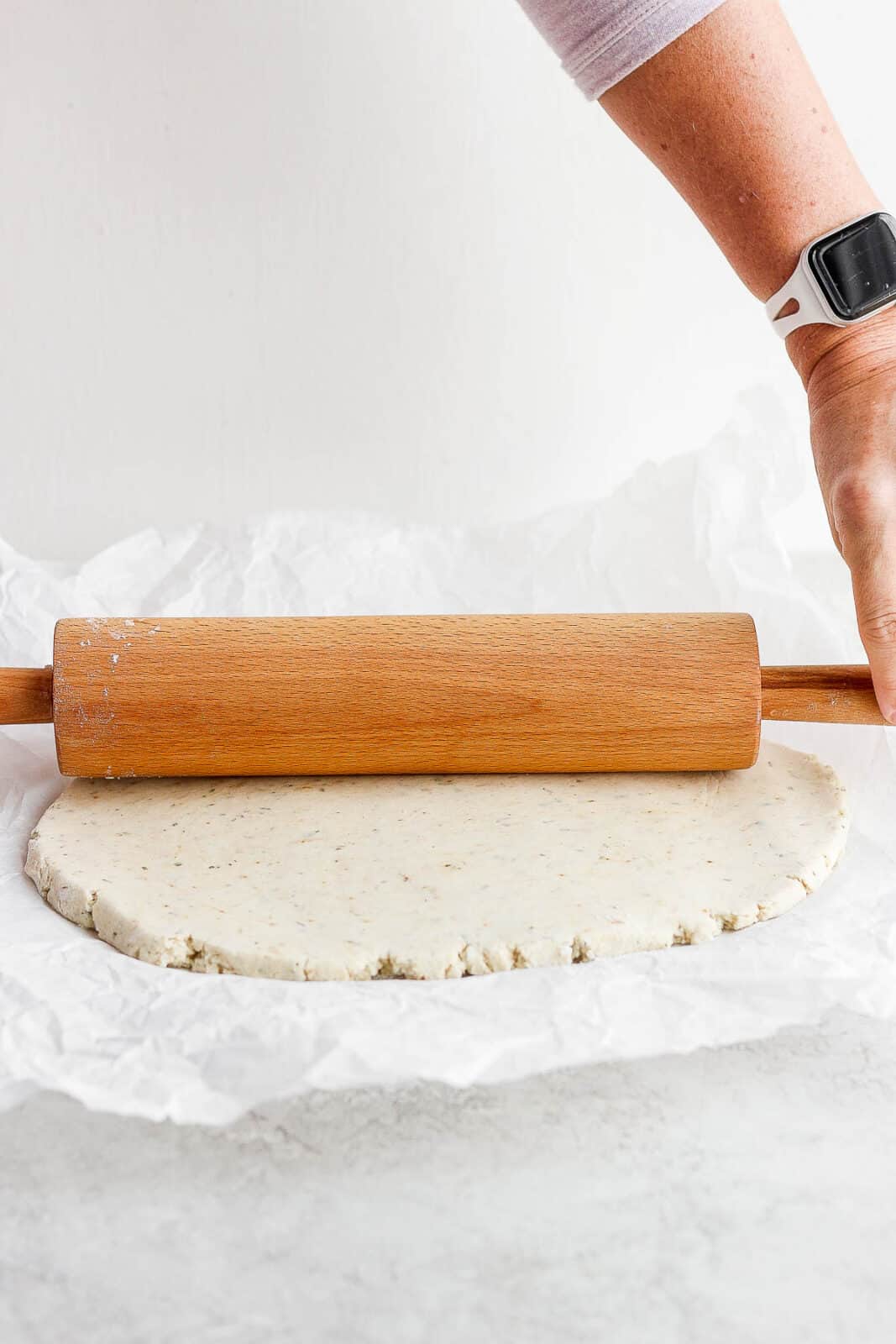 Gluten free biscuit dough being rolled out with a rolling pin.