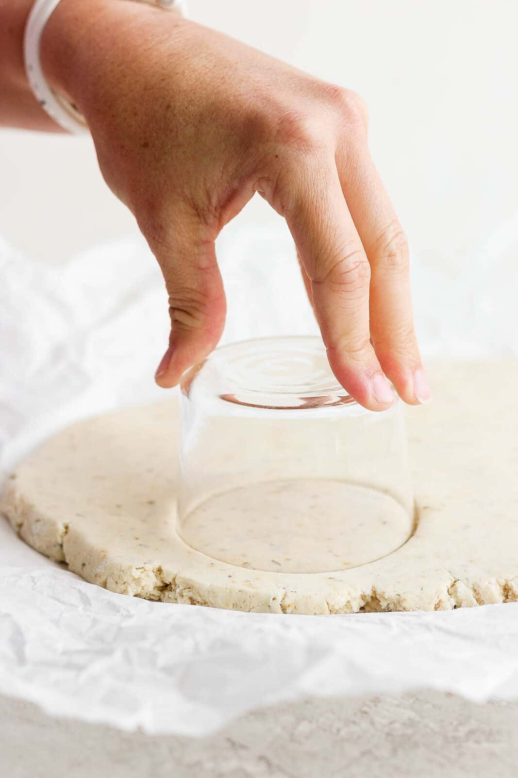 Gluten free biscuit dough being cut into circles with a small glass.