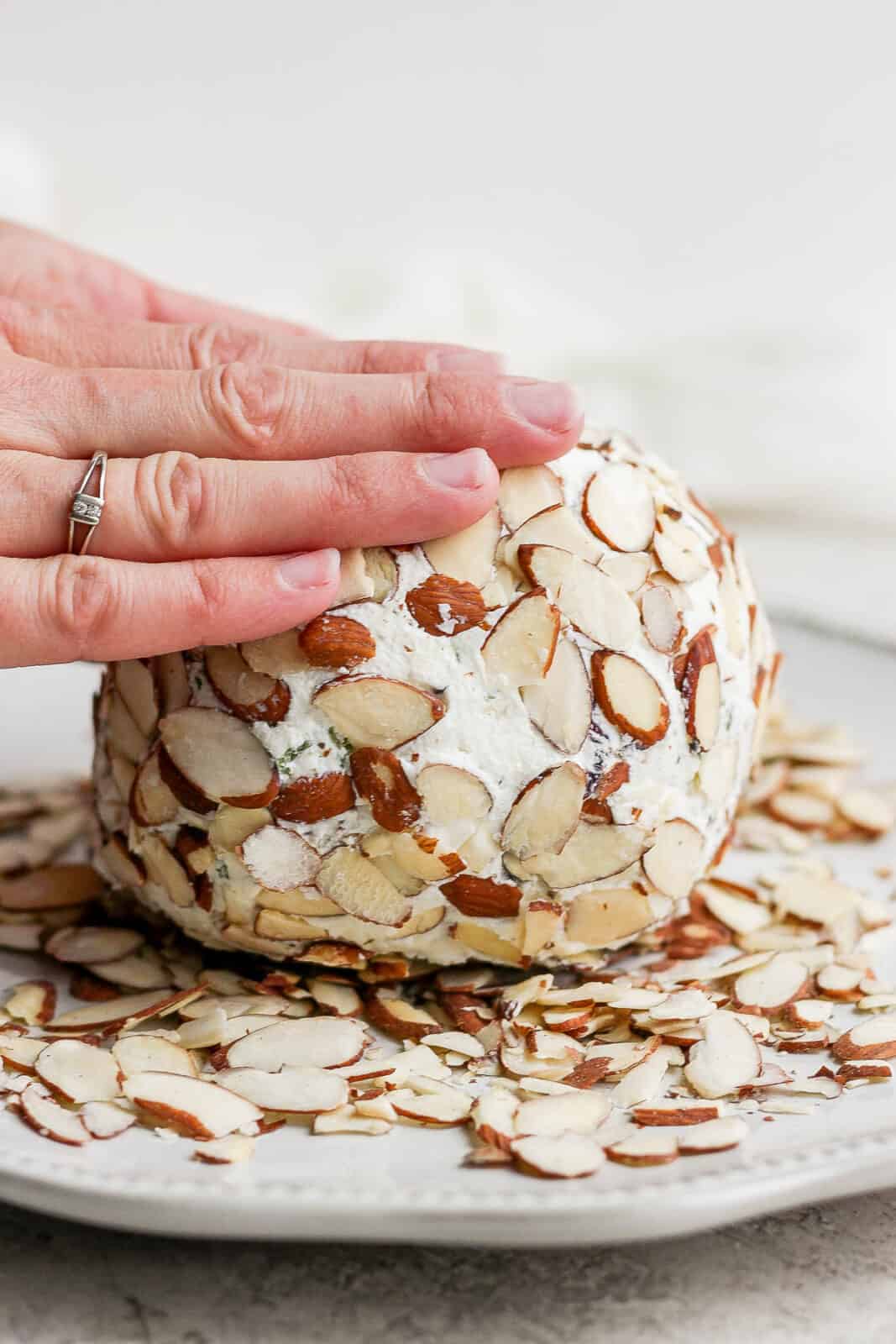 Hands rolling the goat cheese ball in slivered almonds.