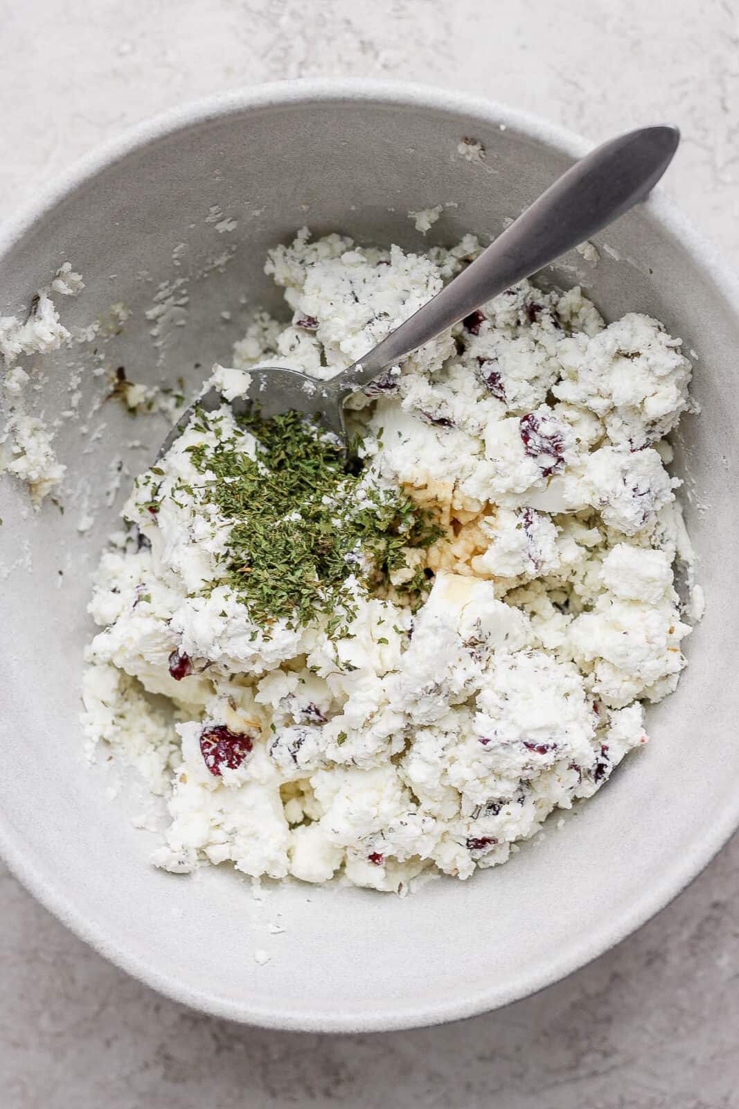 A fork mixing the goat cheese ball ingredients in a bowl.