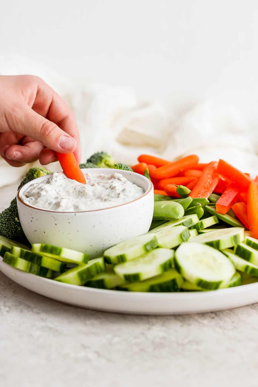 A carrot being dipped in a small dish of healthy veggie dip on a plate of veggies.