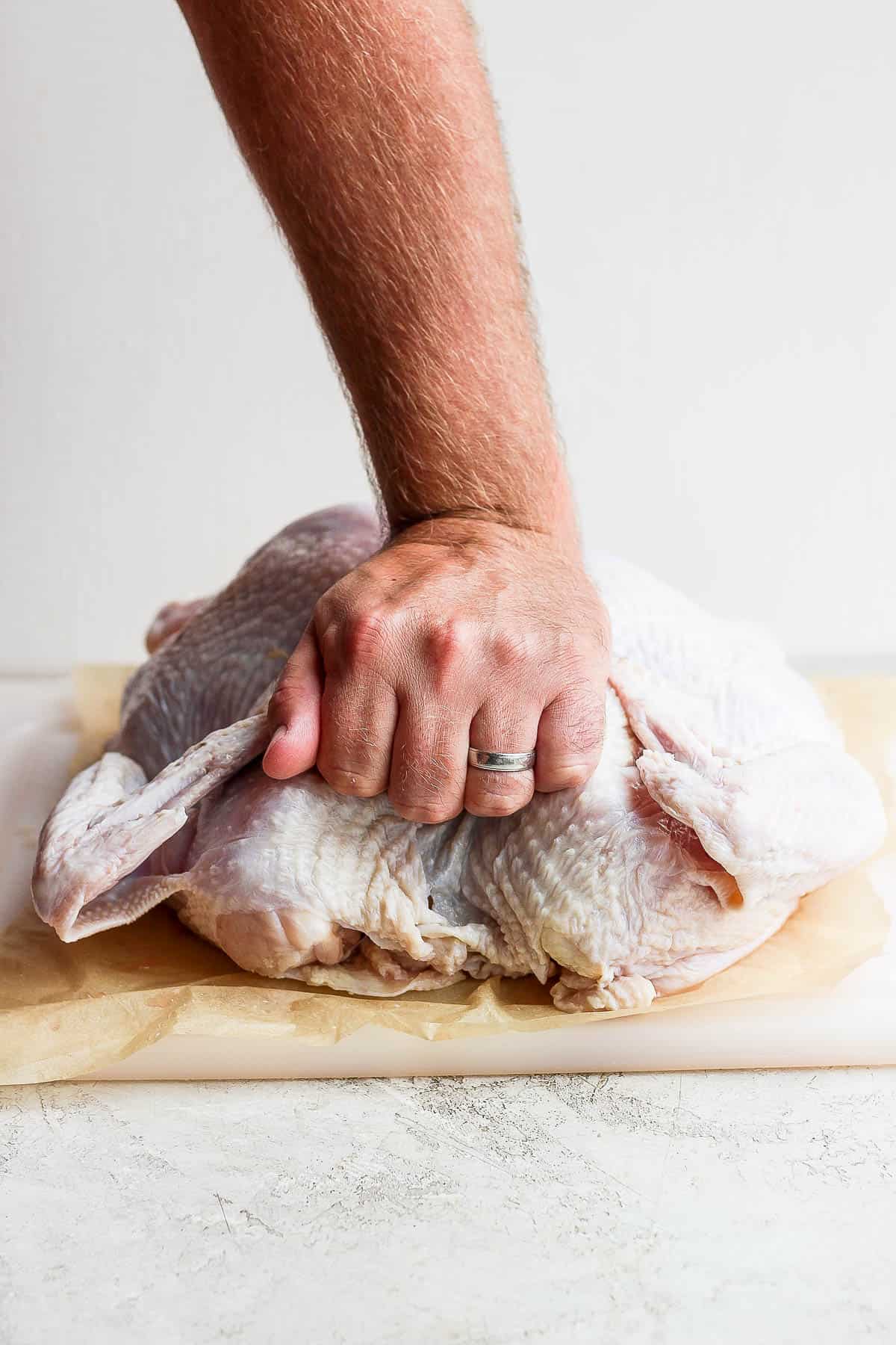 A hand pushing the turkey down so that it lays flat.