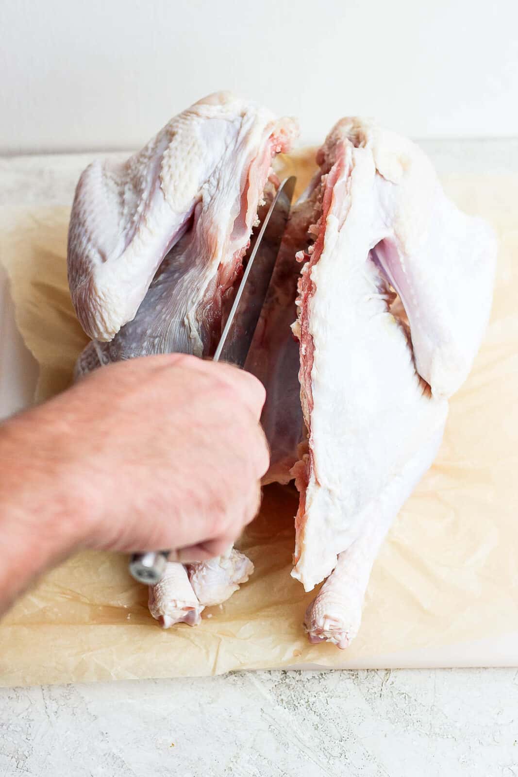 Someone using a knife to make a slit at the top of the breastbone so the chicken can be flipped and lay flat.