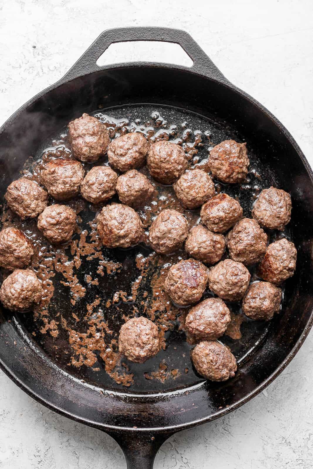 Meatballs cooking in a cast iron skillet.