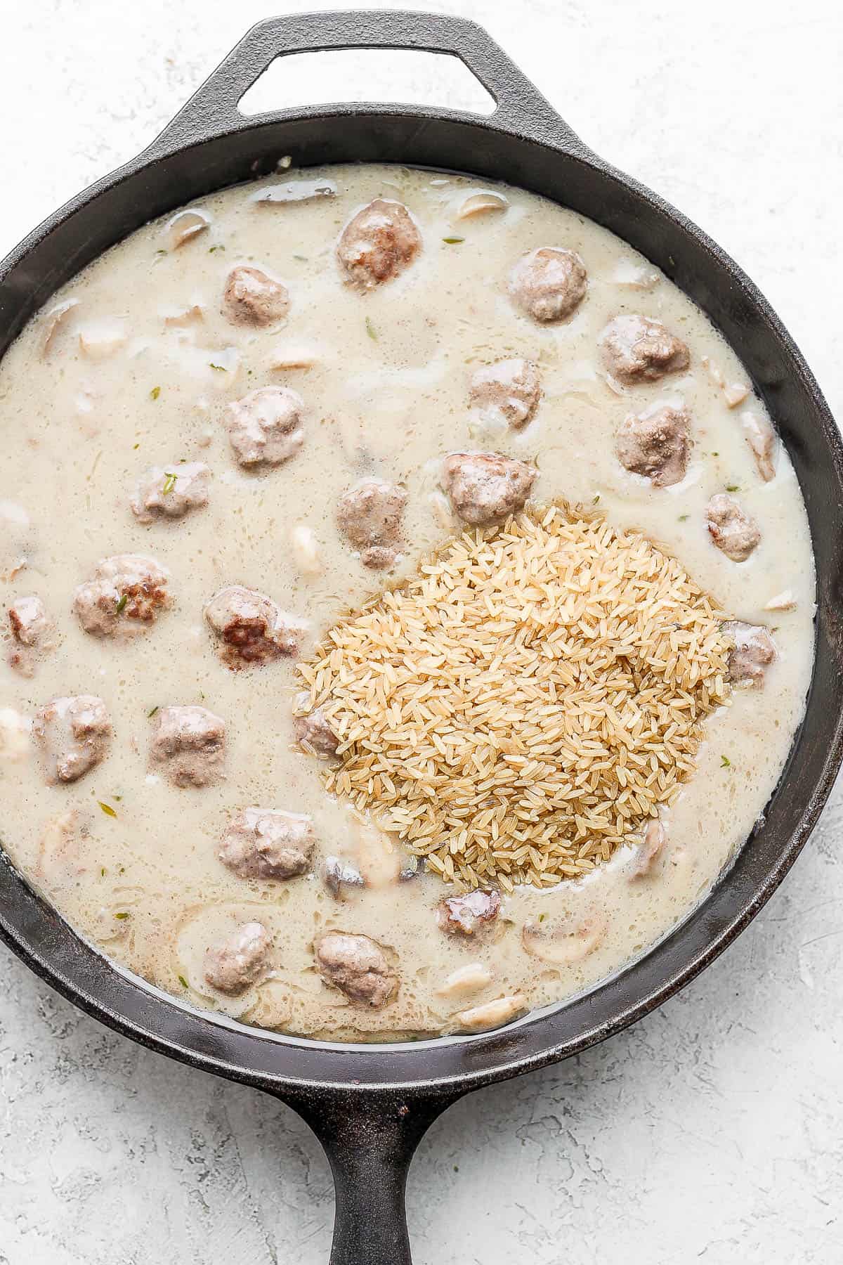 Meatballs and cream of mushroom soup in a cast iron skillet with rice added.