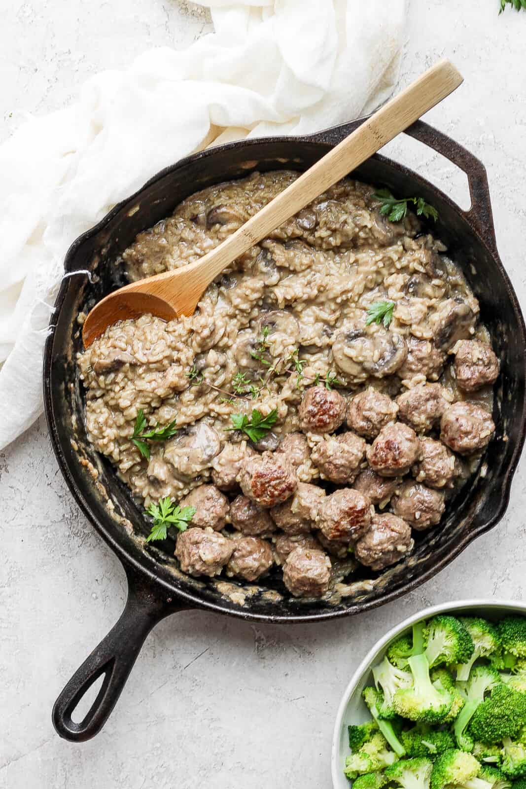 Meatballs and rice in a cast iron skillet plus a side of broccoli.