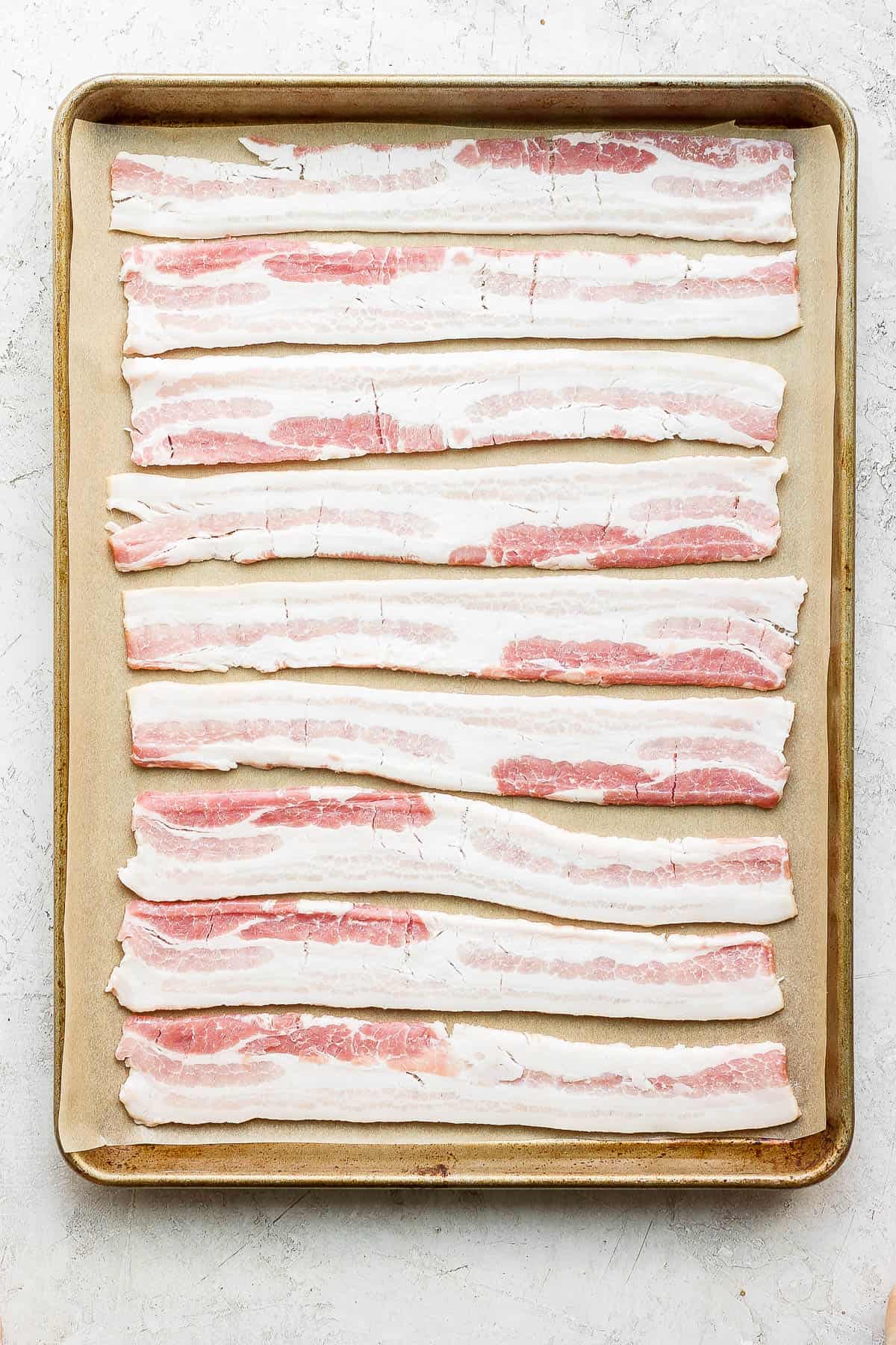 Uncooked bacon on a parchment-lined baking sheet.