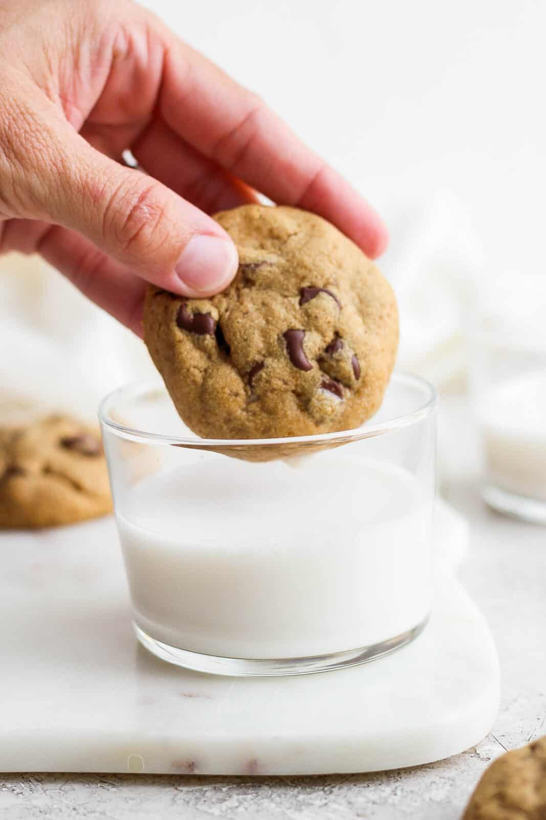 A paleo chocolate chip cookie being dipped into a glass of milk.