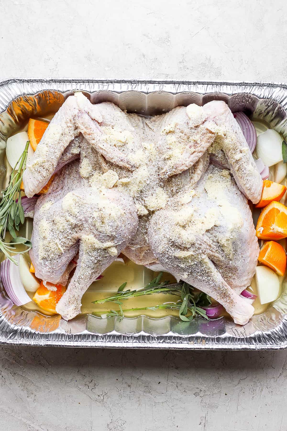 A brined turkey that has been spatchcocked and prepped in a roasting pan.