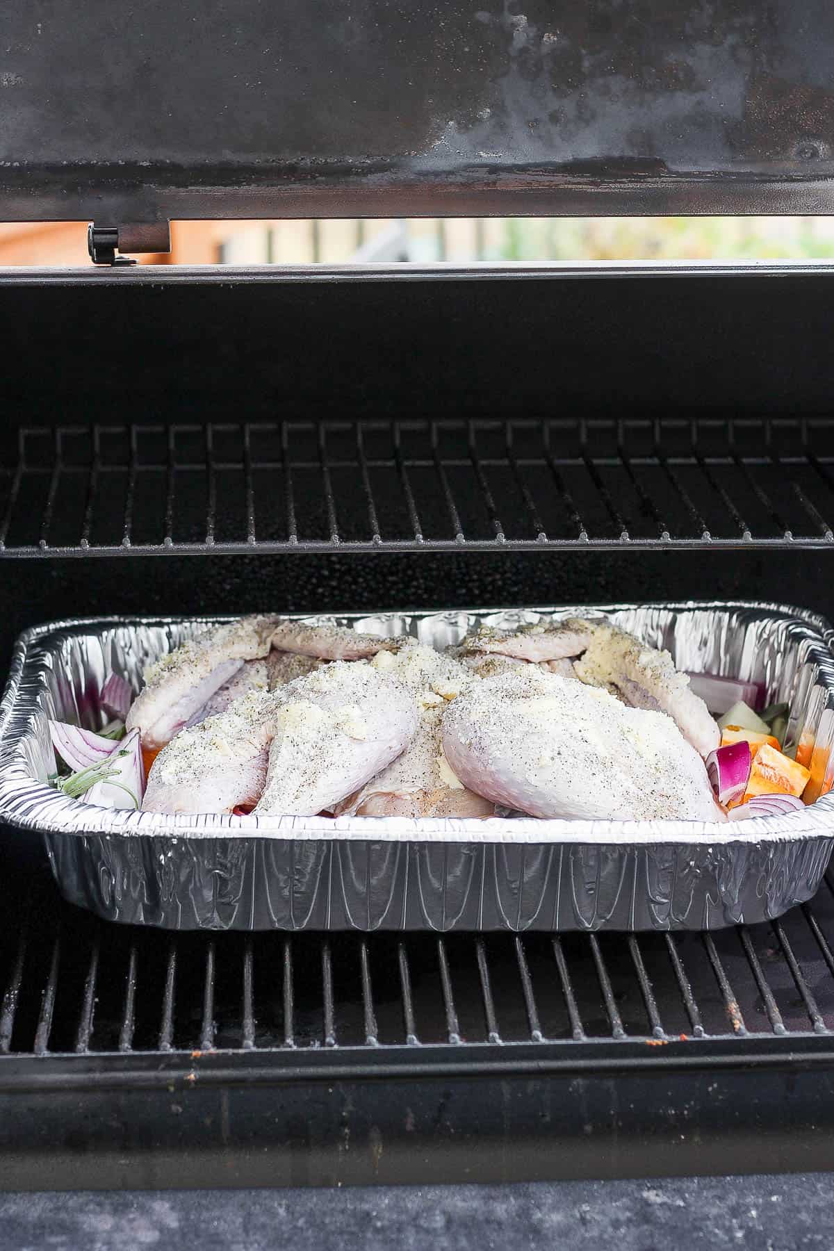 A spatchcocked turkey in a roasting pan on a smoker. 