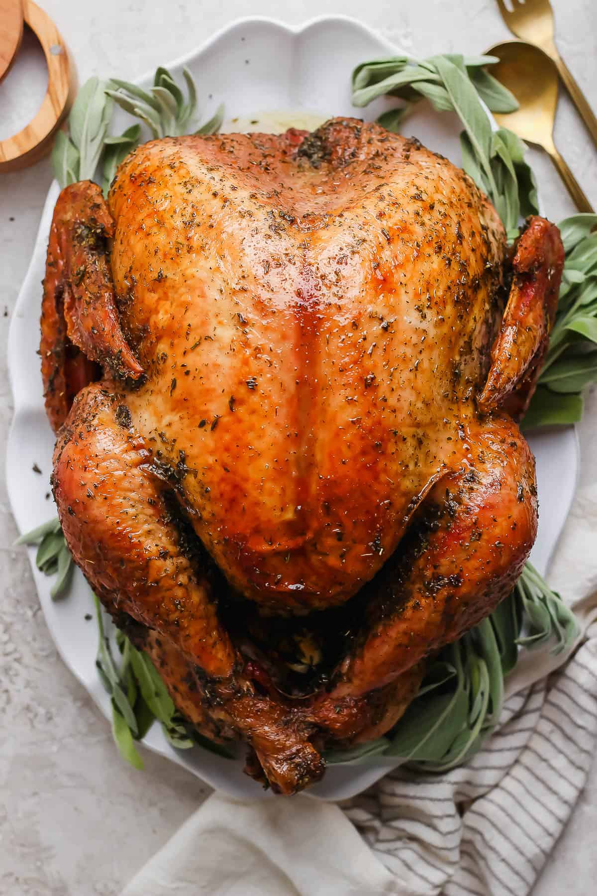A whole, cooked turkey on a platter with fresh herbs around it.