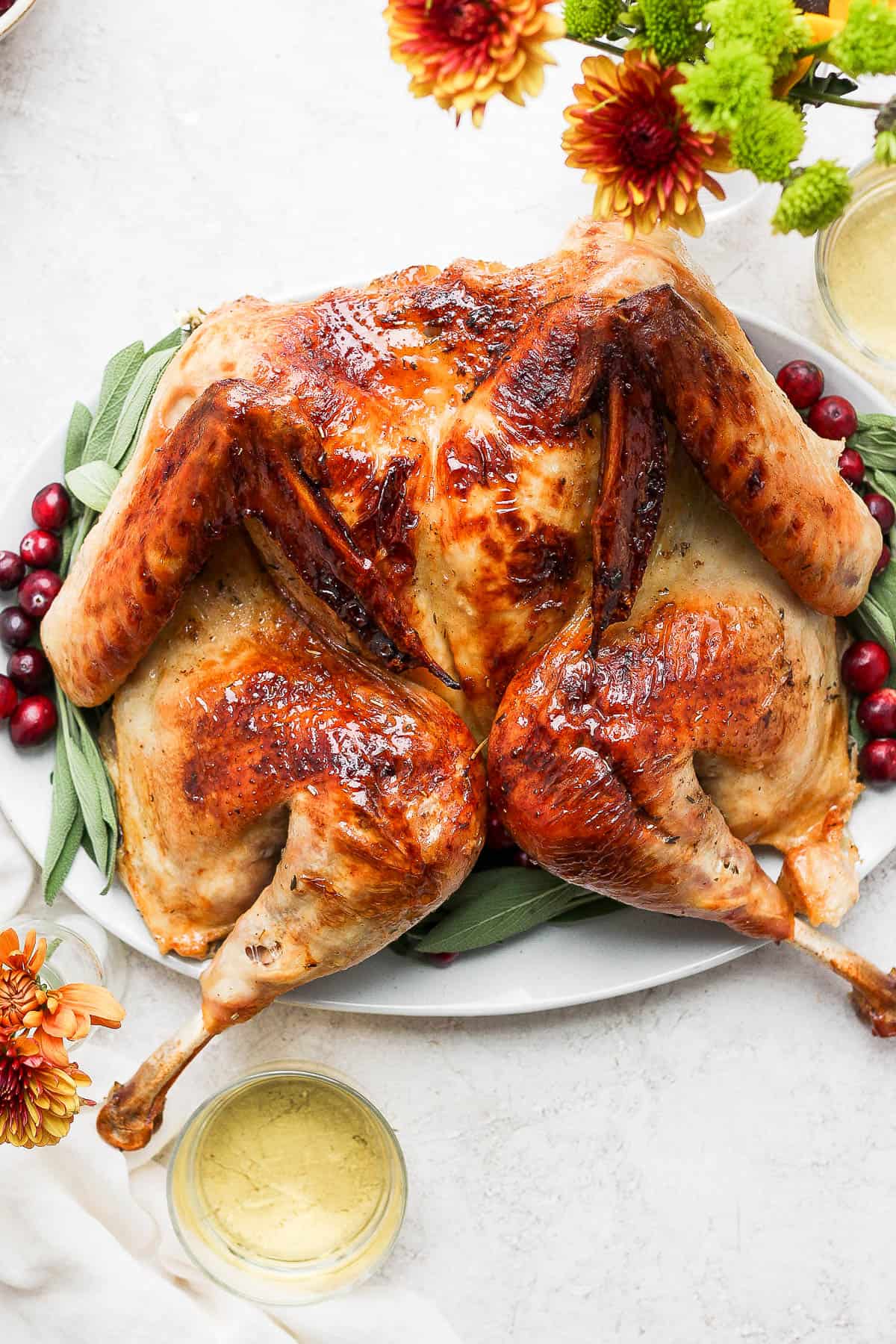 A spatchcock turkey on a platter with cranberries and fresh sage. 