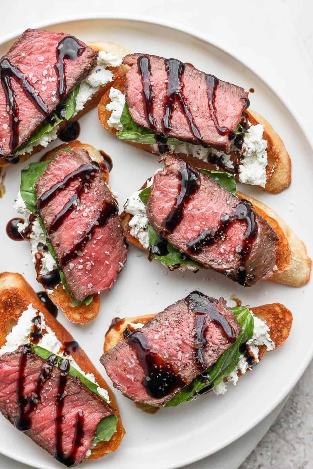 A plate of steak crostini with goat cheese, basil and balsamic glaze. 