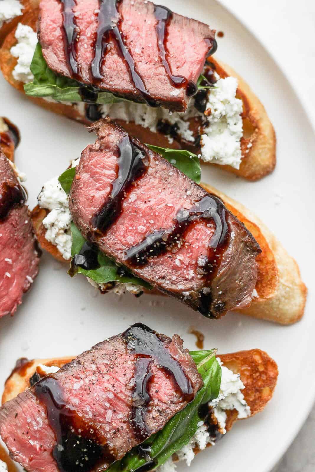 A plate of steak crostini with goat cheese, basil and balsamic glaze. 