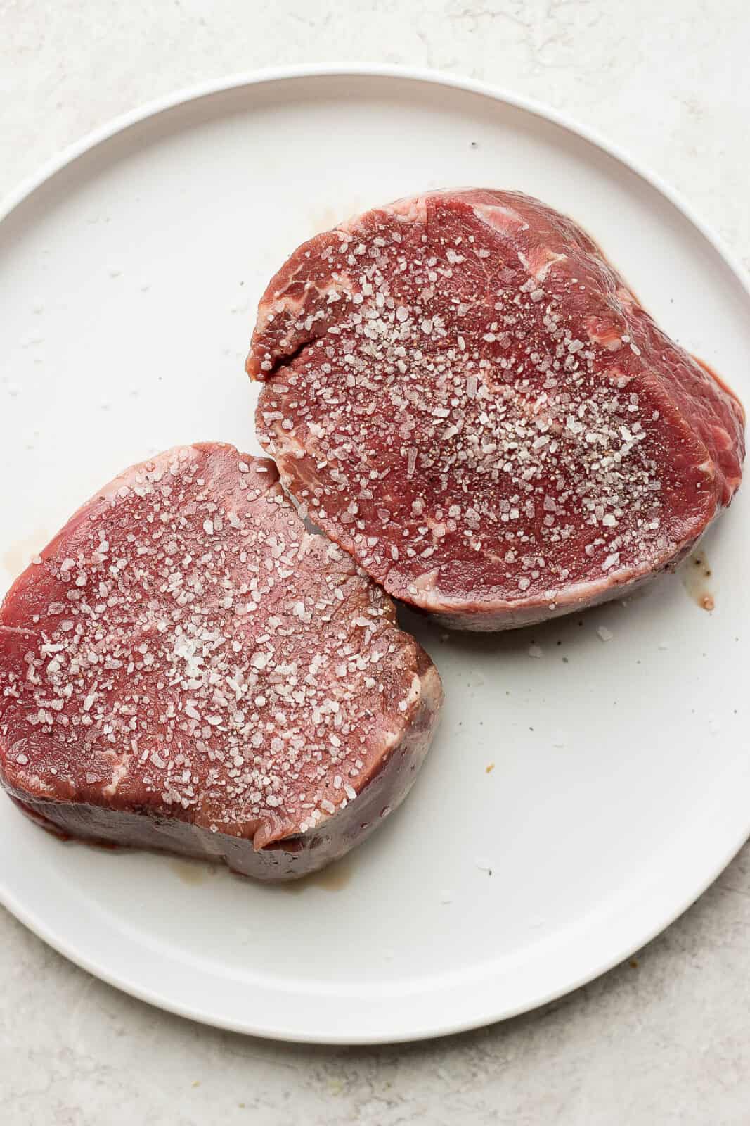 A plate with two sirloin steaks on it seasoned with salt and pepper.