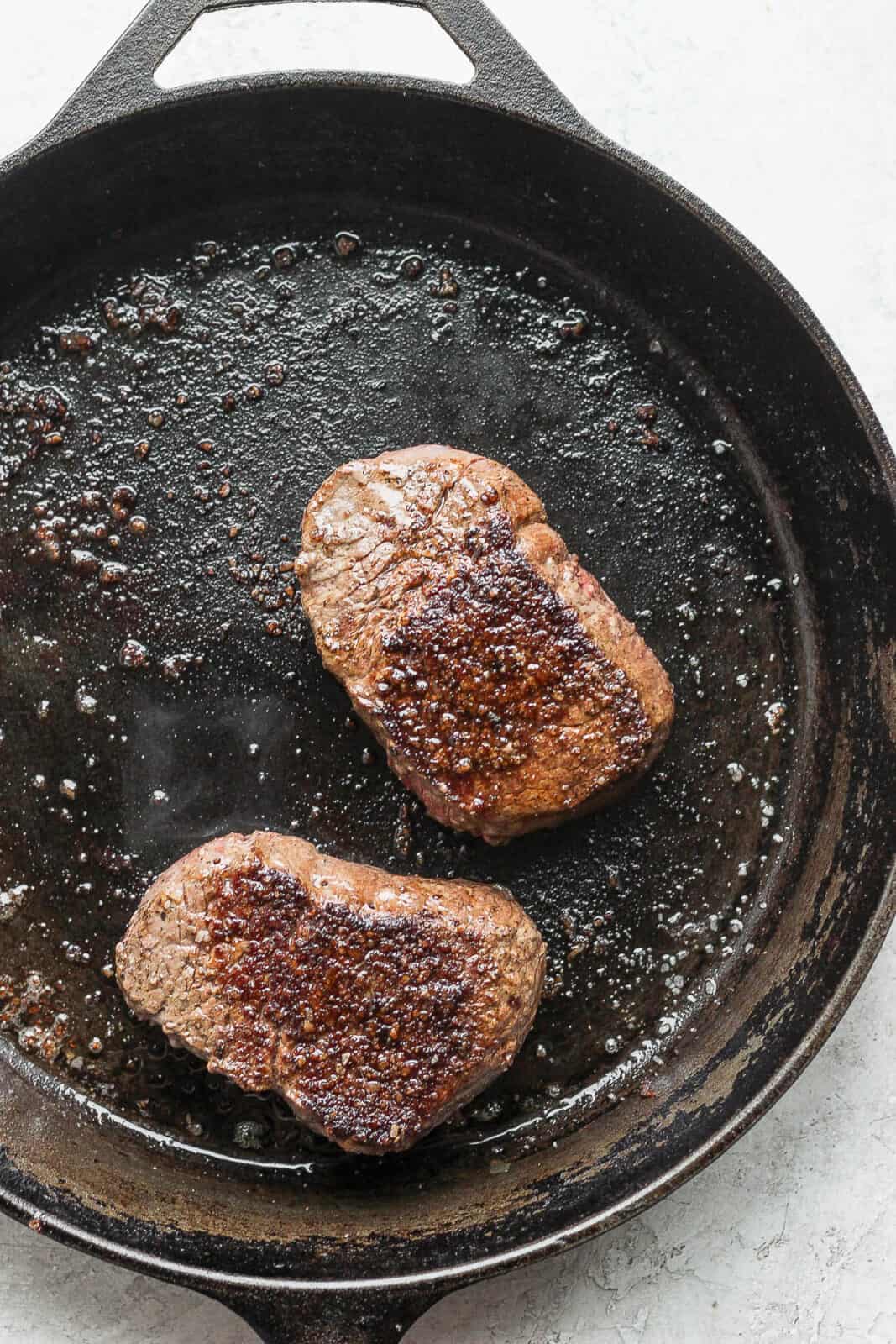 Two sirloin steaks in a cast iron skillet.