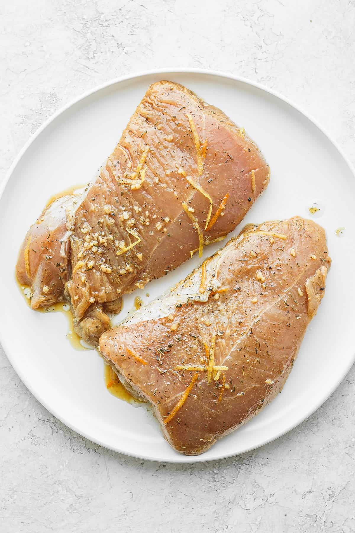 Two pieces of turkey, marinated, on a plate. 