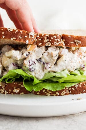 Turkey salad in a sandwich with someone pulling up a corner of a piece of bread.