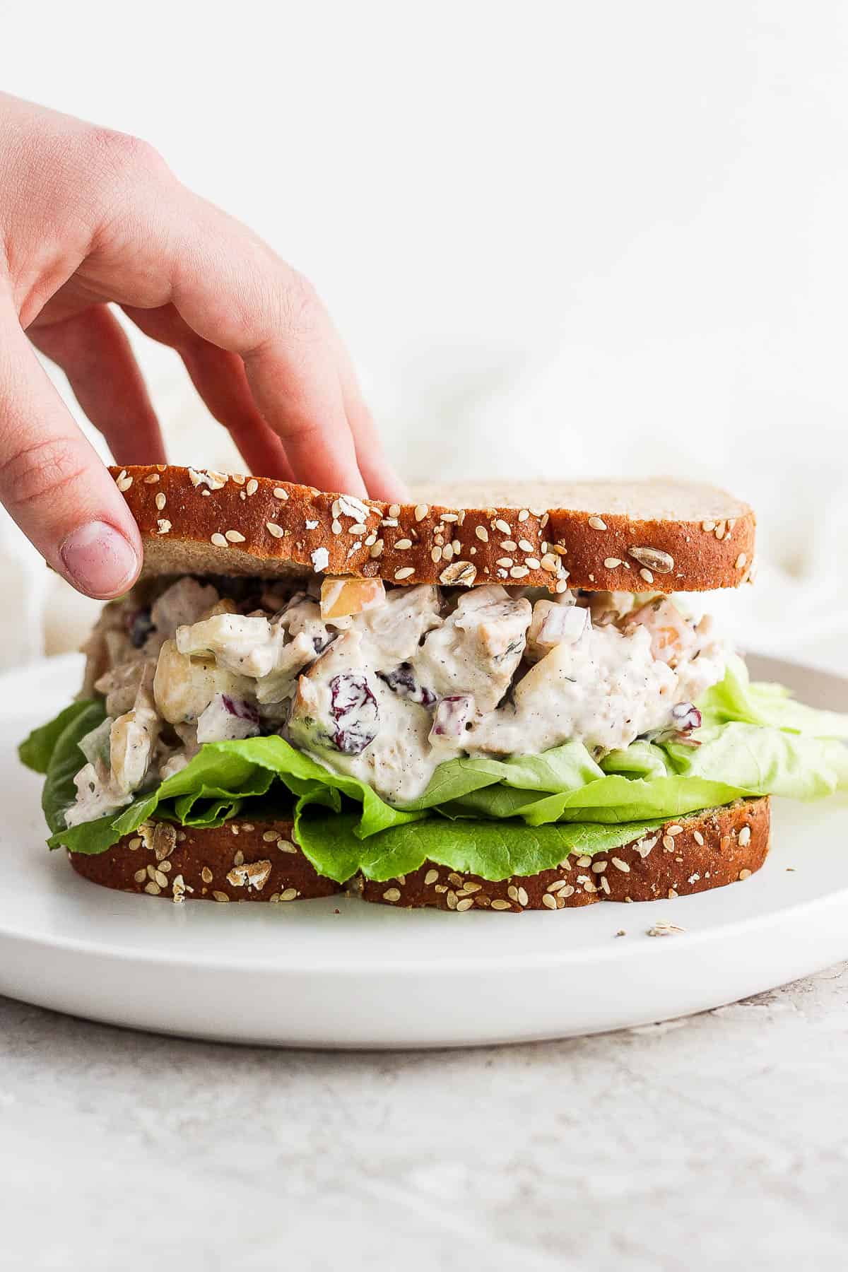 A hand placing the top piece of bread on a turkey salad sandwich.