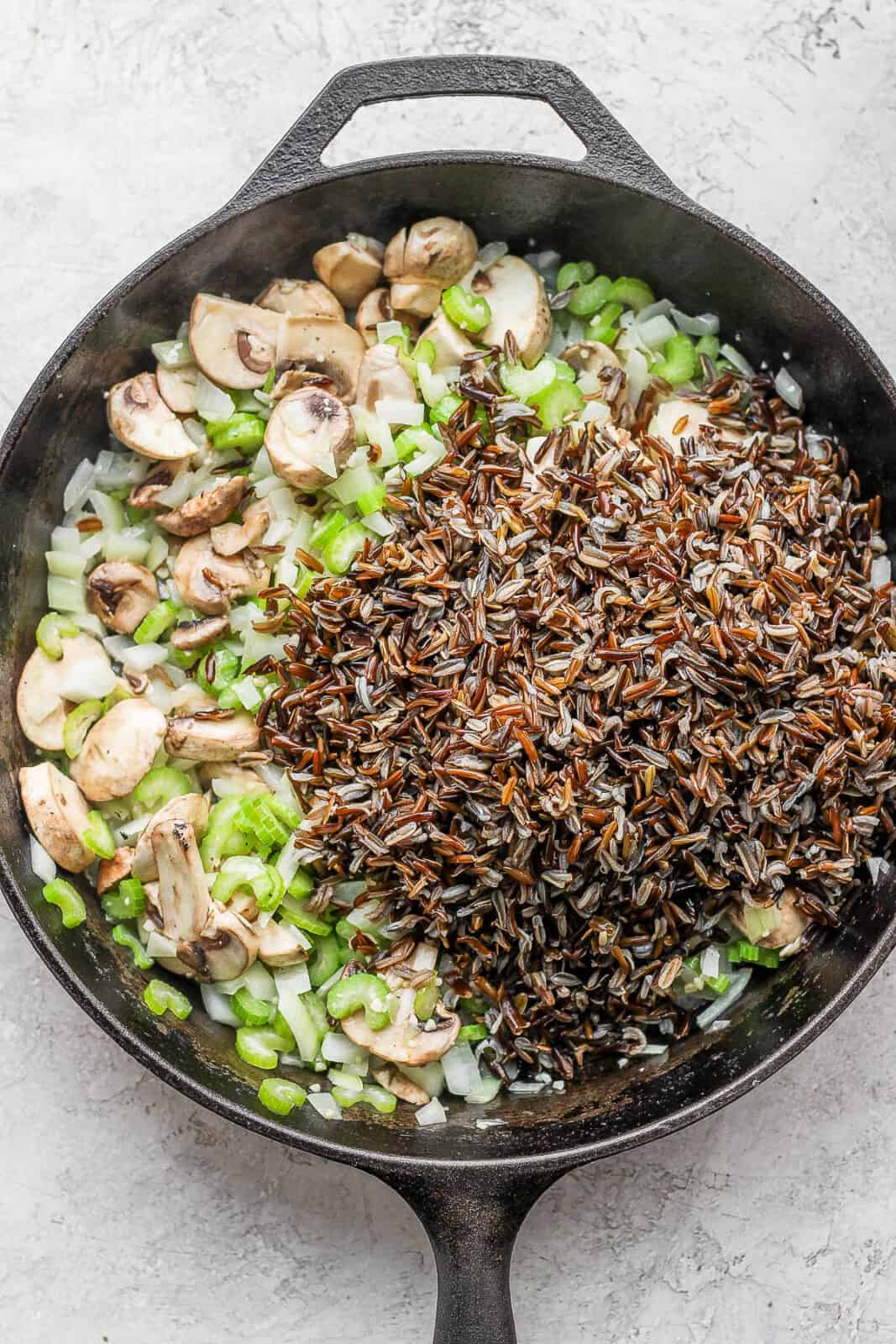 Cast iron skillet with onion mixture, mushrooms, and cooked wild rice.