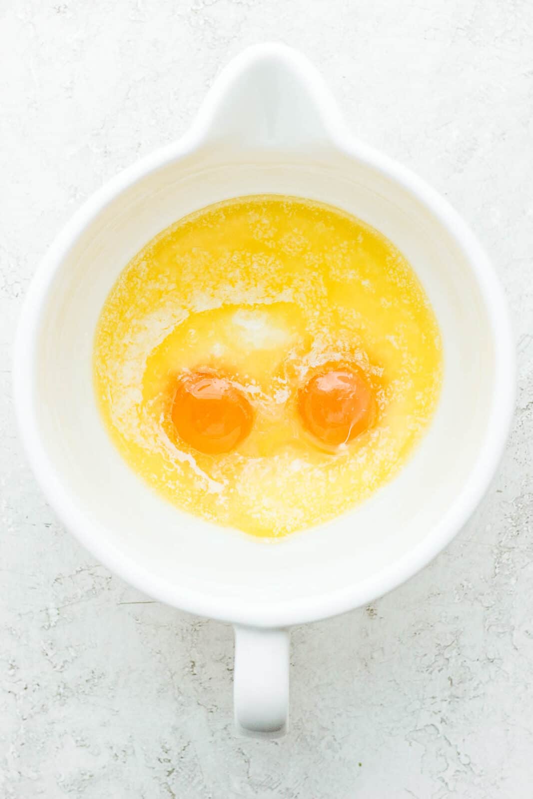 Butter melted in a bowl along with some almond milk and two eggs.