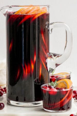 A pitcher of Christmas Sangria with a smaller glass beside it.